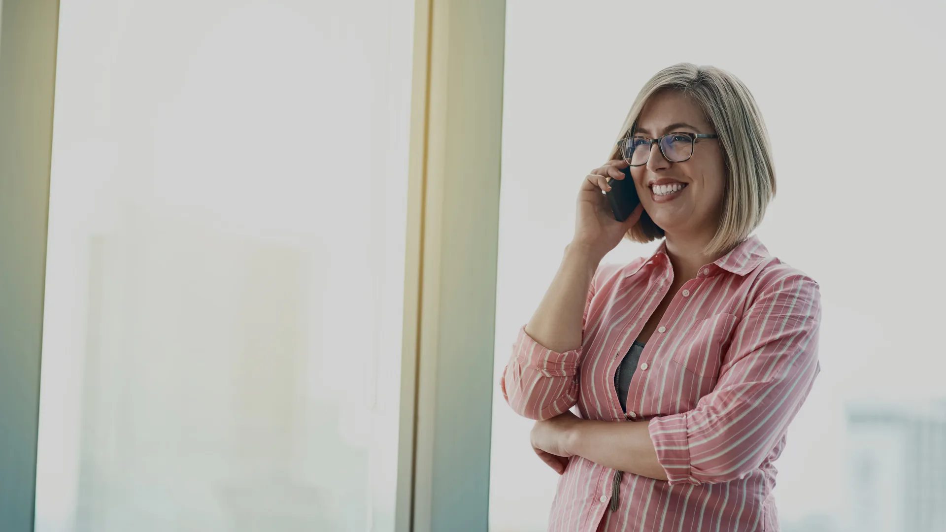 Una responsabile sui quarantacinque, in piedi alla vetrata satinata di un ufficio, con il telefono all’orecchio: sorride ascoltando, le braccia conserte.