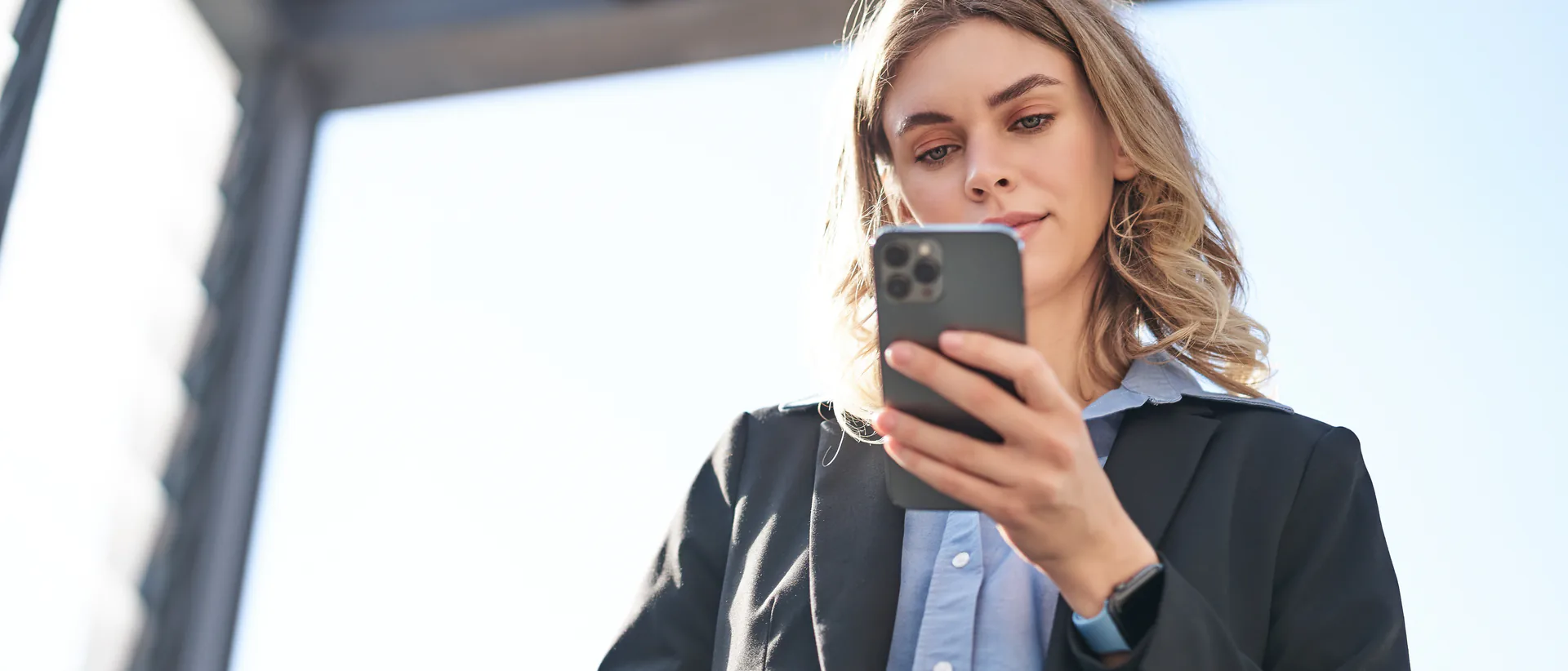 Una donna d'affari in giacca scura, su una scala mobile in città, legge un messaggio sul proprio telefono in controluce e sorride appena